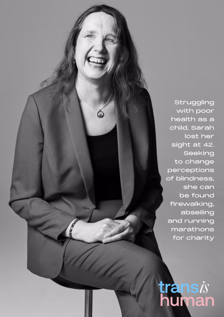 Black and white portrait of a woman sitting down with the caption “Struggling with poor health as a child, Sarah lost her sight at 42. Seeking to change perceptions of blindness, she can be found firewalking, abseiling, and running marathons for charity. Trans is human”.